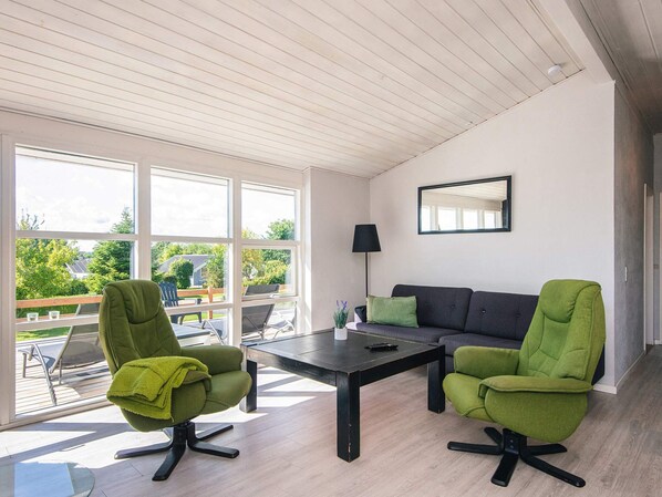 A modern living room with a sofa, two armchairs, a coffee table, and a large window offering a view of the outdoors.