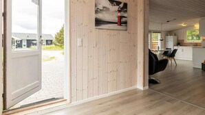 A modern interior with a wooden panel wall, a dining area with black chairs, and a kitchen with white cabinets. - Spacious Holiday Home in Strøby near Beach (Aalbaek)