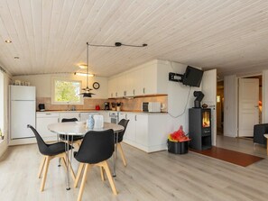 A modern kitchen with white cabinets, a round dining table with black chairs, a built-in stove, and a flat-screen TV mounted on the wall. - Spacious Holiday Home in Strøby near Beach (Aalbaek)