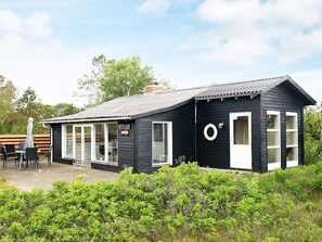 A small black wooden building with a white door and windows, a covered patio area with chairs, and a sign that reads 'Milton'. - Spacious Holiday Home in Strøby near Beach (Aalbaek)
