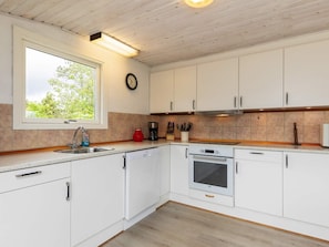 A modern kitchen with white cabinets, a dishwasher, an oven, and a window with a view of greenery. - Spacious Holiday Home in Strøby near Beach (Aalbaek)
