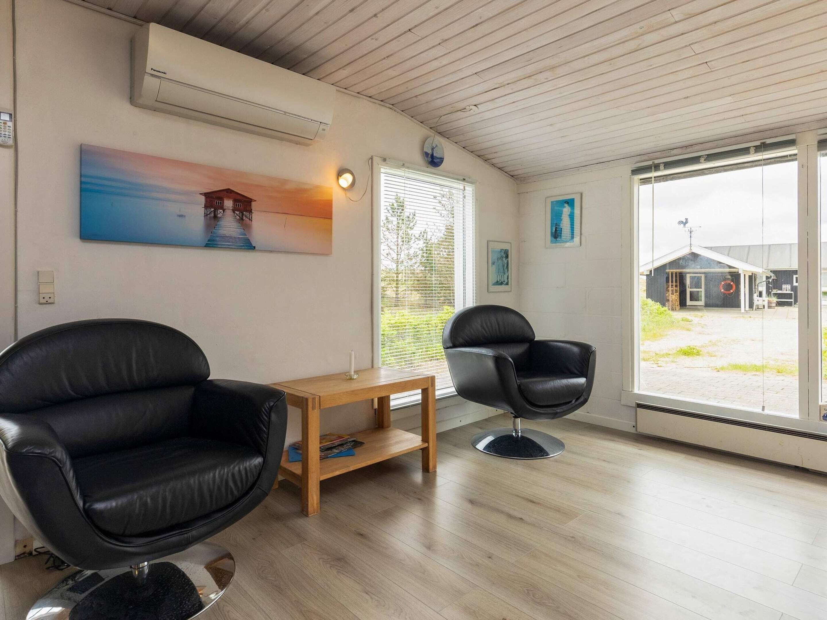 A room with a wooden ceiling, a black leather chair, a wooden table, and a large window with blinds.