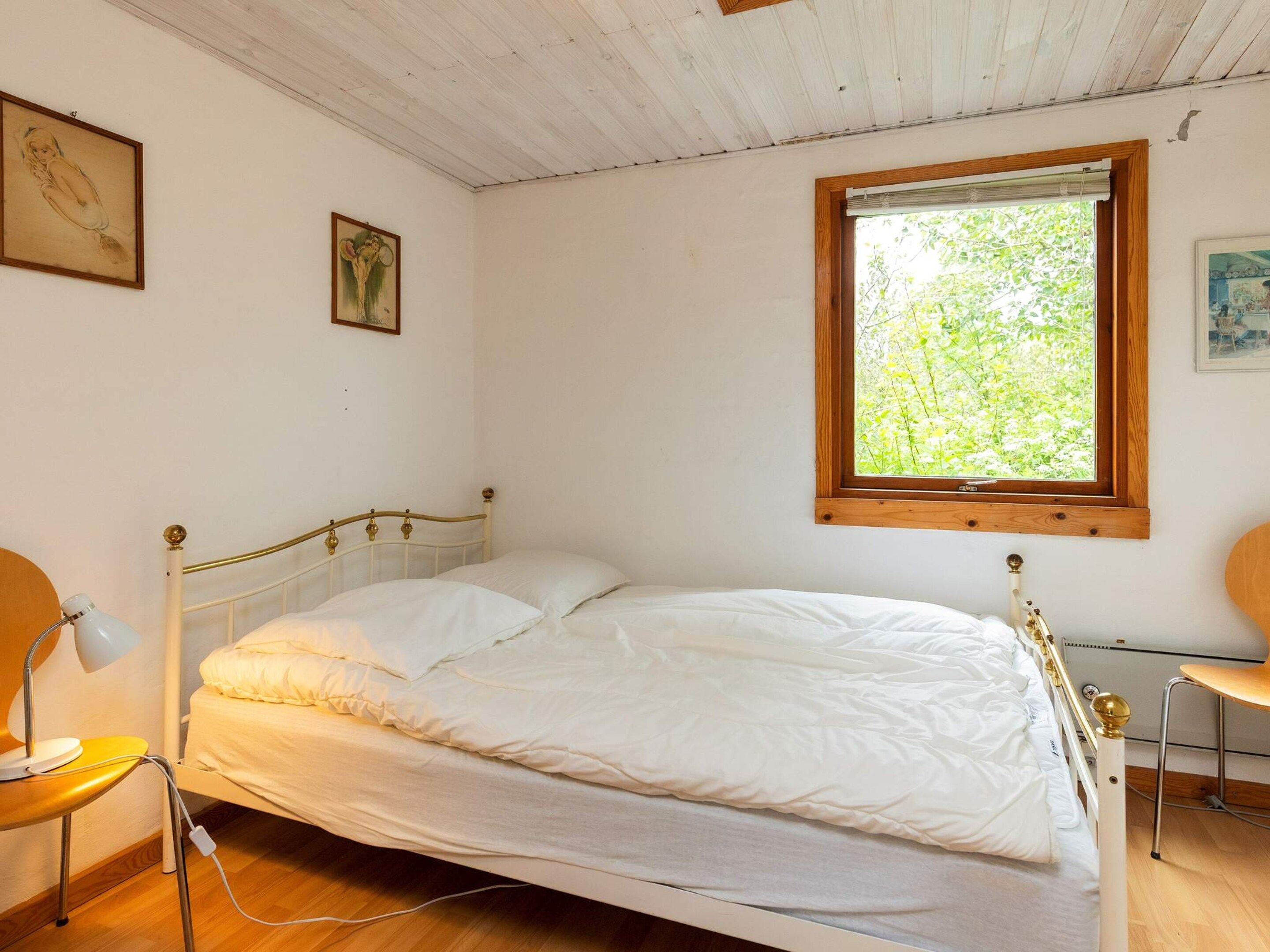 Un lit simple avec une tête de lit en bois, une table de chevet avec une lampe et une fenêtre donnant sur un paysage verdoyant.