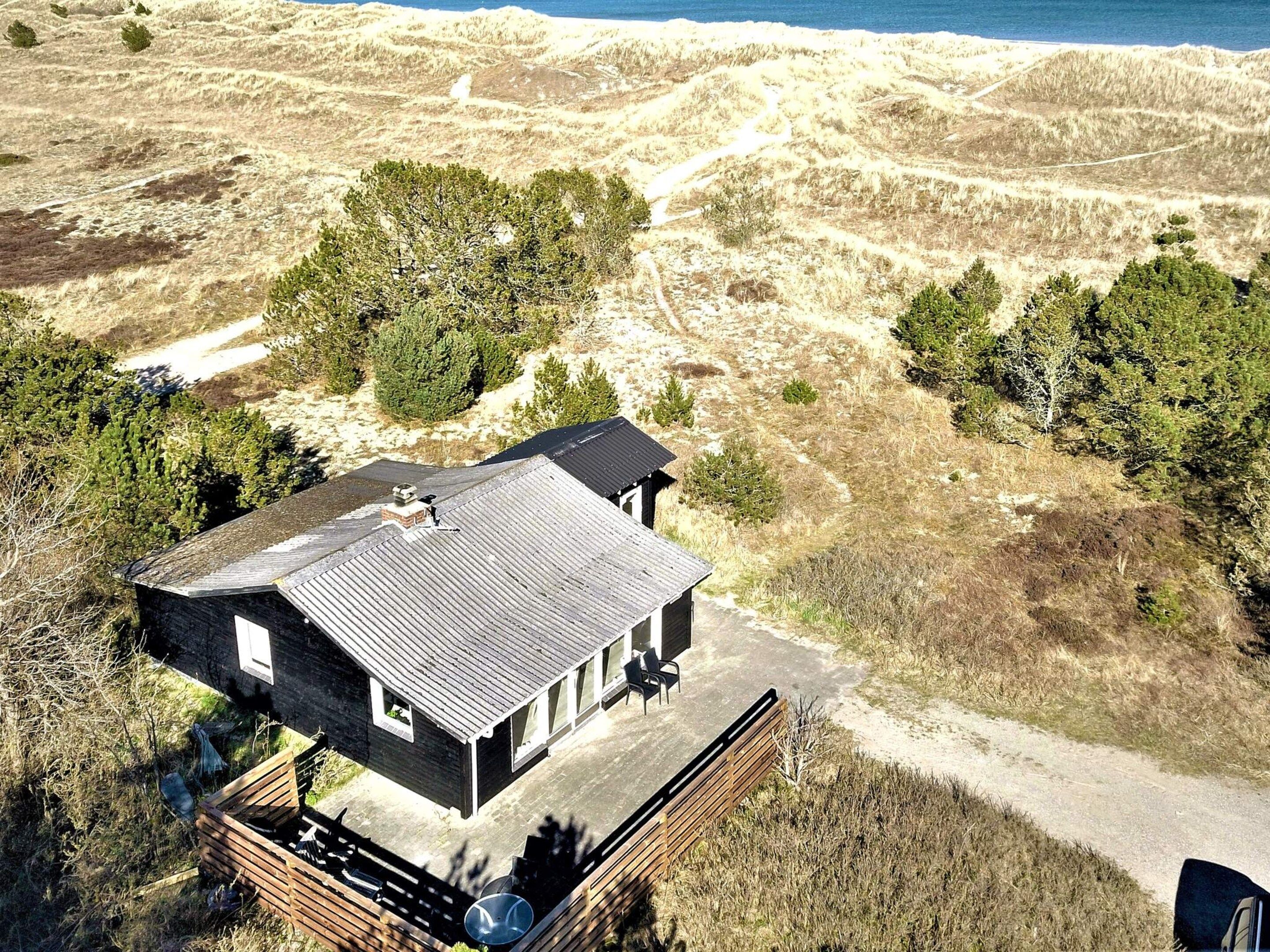 A modern house with a sloped roof, a deck, and a view of the surrounding dunes and ocean.