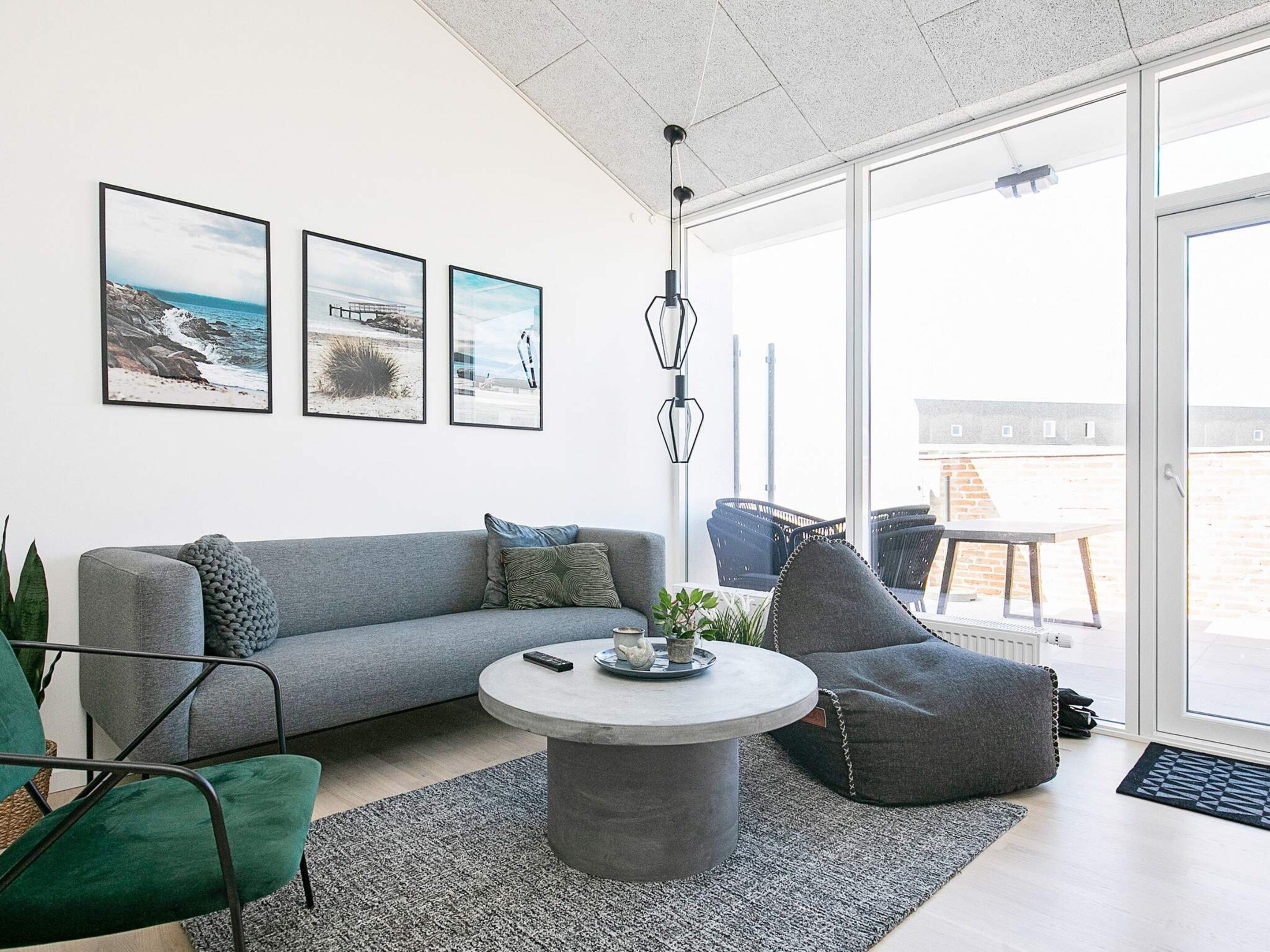 A modern living room with a grey sofa, a round coffee table, and a large window offering a view of the outdoors.