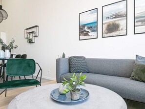 A modern living room with a grey sofa, green chairs, a round coffee table with plants, and framed artwork on the wall. - Cozy Holiday Home in Syddanmark near Beach (Ringkobing)