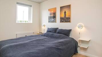 Un dormitorio con una cama grande, dos lámparas de noche, un ventanal y dos cuadros colgados en la pared.