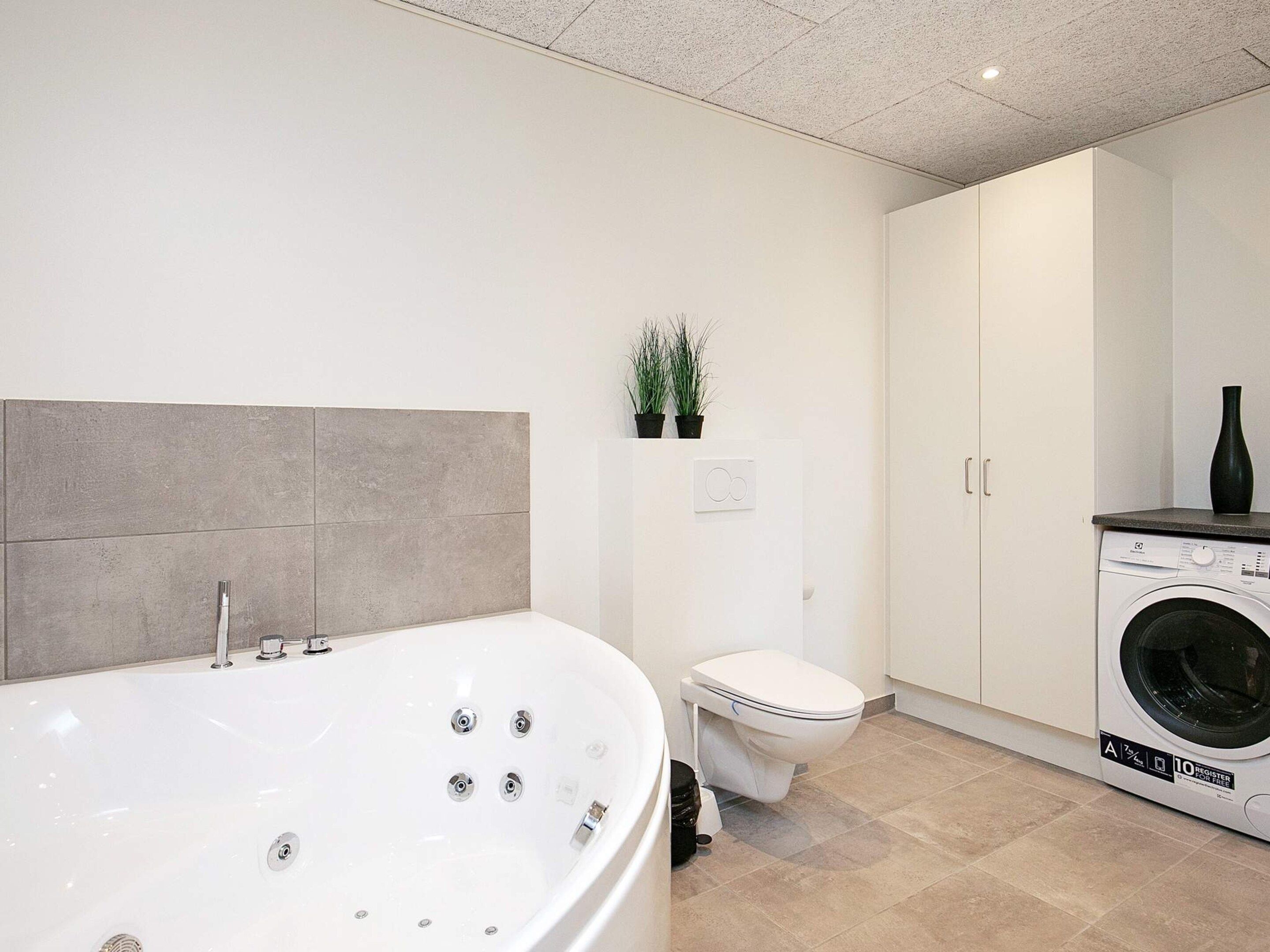 A modern bathroom with a freestanding bathtub, a toilet, a washing machine, and a cabinet.