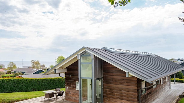 A modern house with a sloped roof, a glass door entrance, and a wooden deck. - 6 Person Holiday Home in Hejls (Hejls)