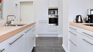 A narrow kitchen with white cabinets, a microwave, an oven, and a coffee maker on the counter. - 6 Person Holiday Home in Hejls (Hejls)