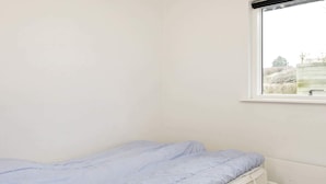 A small, single-bed room with a window, white walls, and a plain bedspread. - 6 Person Holiday Home in Hejls (Hejls)