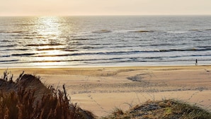 A beach with a person riding a bicycle, waves, and the sun setting over the ocean. - 4 Star Holiday Home in Ringkobing (Ringkobing)