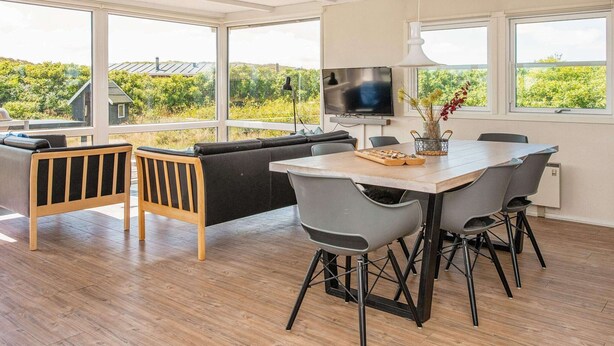 A modern dining area with a wooden table, grey chairs, and a TV. - 4 Star Holiday Home in Ringkobing (Ringkobing)