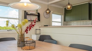 A modern kitchen with a wooden table, a vase with red flowers, and a wooden tray with stones. - 4 Star Holiday Home in Ringkobing (Ringkobing)