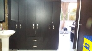 Une pièce avec une grande armoire sombre, un lavabo blanc et une porte donnant sur un espace extérieur.