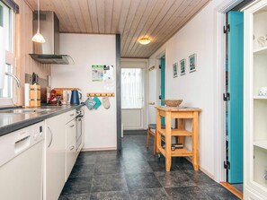 Cocina moderna con lavavajillas, pileta y armarios de madera. Hay un comedor con mesa y sillas, y una puerta azul que conduce a otra habitación.