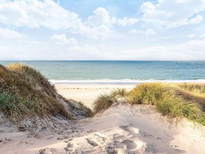 En strand med klitter og fodaftryk, der fører hen til vandet.