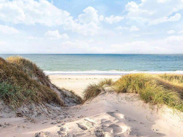A beach with sand dunes and footprints leading to the water.