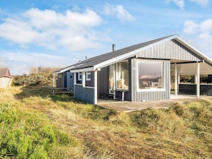A modern beach house with a covered patio, large windows, and a wooden deck.