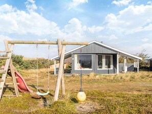 Une maison moderne avec une balançoire et un toboggan, installés dans un champ d’herbe.