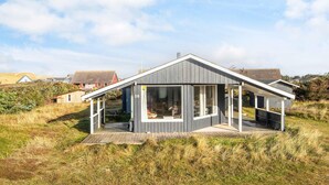 Une maison moderne dotée d’une grande baie vitrée, d’une terrasse en bois et d’une plaque portant le numéro 16.