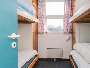 A bunk bed room with a window, a radiator, and a door.