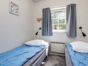 A small, simple room with two single beds, a window with curtains, a wall-mounted lamp, and a framed picture. - 4 Star Holiday Home in Vaeggerlose (Vaeggerlose)