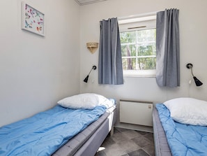 A room with two single beds, a window with curtains, a wall-mounted lamp, and a framed picture. - 4 Star Holiday Home in Vaeggerlose (Vaeggerlose)