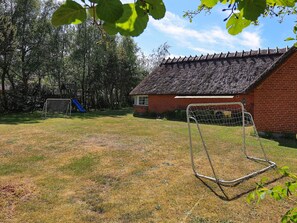 A brick building with a thatched roof, a fenced soccer goal, and a playground with a slide.