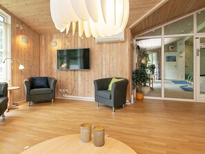 A modern interior with wooden panel walls, a flat-screen TV, two armchairs, a potted plant, and a wooden floor. - 4 Star Holiday Home in Vaeggerlose (Vaeggerlose)