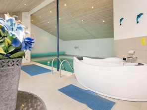 A spa area with a large white bathtub, a blue mat, and a potted plant with blue flowers.