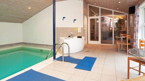 An indoor swimming pool with a jacuzzi, wooden ceiling, and a dining area with chairs and a table. - 4 Star Holiday Home in Vaeggerlose (Vaeggerlose)