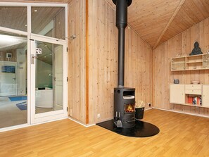 A room with a wood-burning stove, wooden walls, a glass door entrance, and a shelf with books.