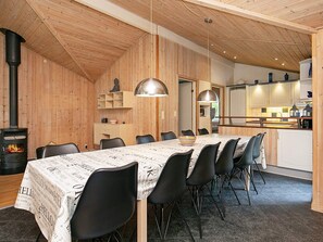 A dining area with a long table, black chairs, and a wood-burning stove. - 4 Star Holiday Home in Vaeggerlose (Vaeggerlose)