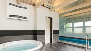 A modern indoor swimming pool with a clear view of the outside through large windows, a built-in hot tub, and a tiled floor. - 4 Star Holiday Home in Blavand (Blavand)
