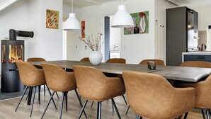 A modern dining area with a central table, chairs, pendant lights, and a wood-burning stove. - 4 Star Holiday Home in Blavand (Blavand)