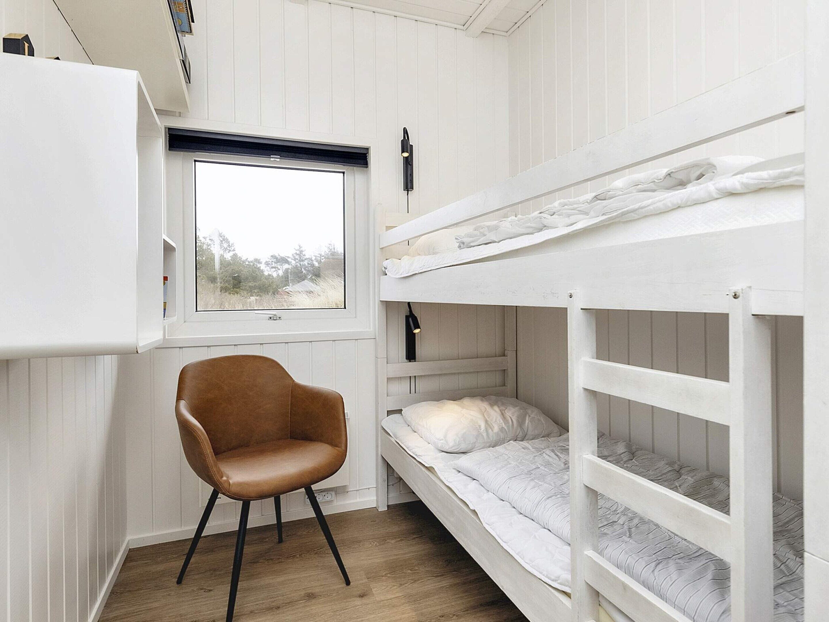 A bunk bed room with a window, a chair, and a white wardrobe.
