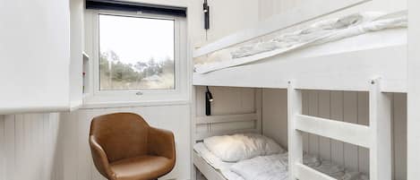 A bunk bed room with a window, a chair, and a white wardrobe.