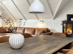 A modern living room with a wooden dining table, a brown leather sofa, a white vase with branches, and a fireplace.