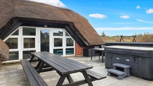 An outdoor patio with a thatched-roof structure, a hot tub, and a picnic table. - 4 Star Holiday Home in Blavand (Blavand)