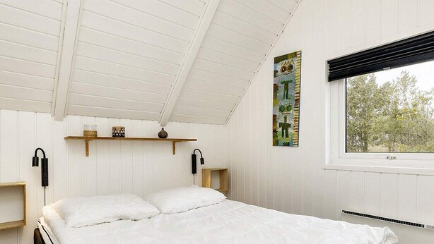 A bedroom with a bed, two bedside tables, a window, and a wall-mounted shelf with decorative items. - 4 Star Holiday Home in Blavand (Blavand)