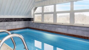 An indoor swimming pool with a clear view of the outdoors through large windows. - 4 Star Holiday Home in Blavand (Blavand)