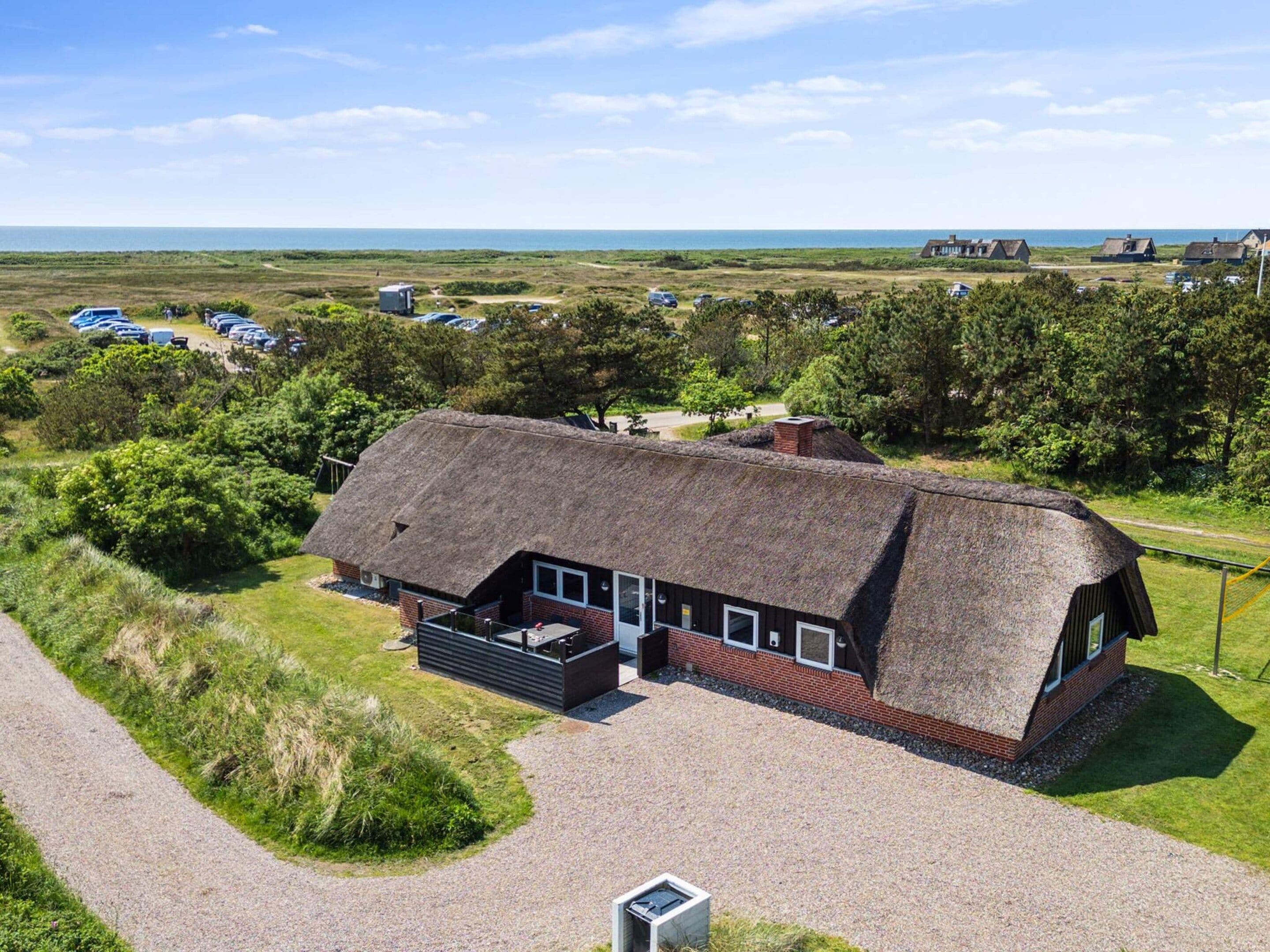A thatched-roof building with a gravel driveway, surrounded by greenery and a parking area.