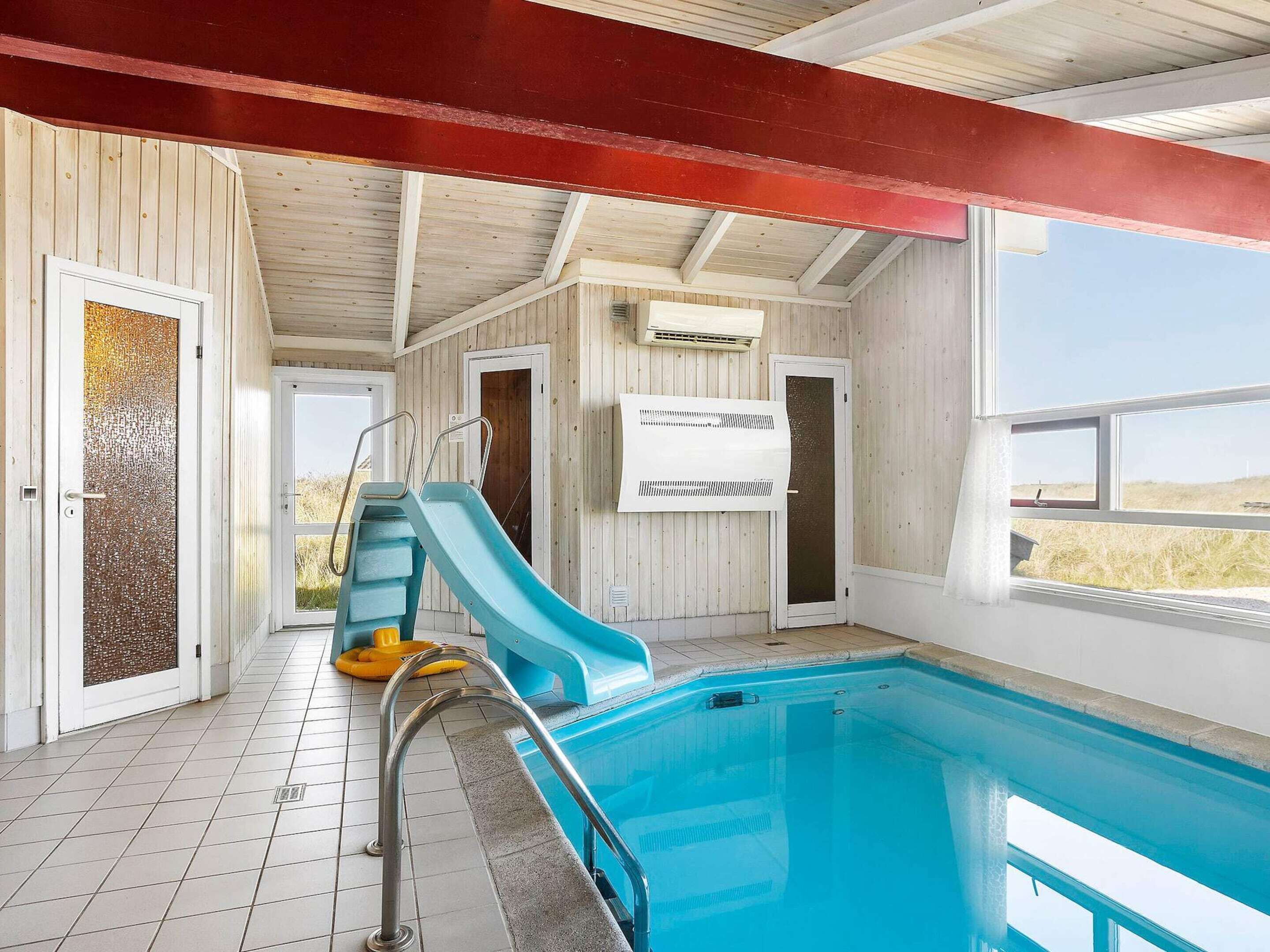 A swimming pool with a slide, tiled floor, and wooden walls.