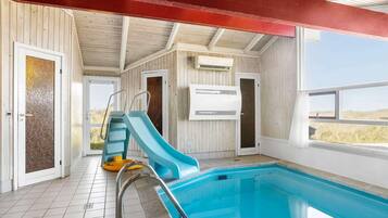 A swimming pool with a slide, tiled floor, and wooden walls.