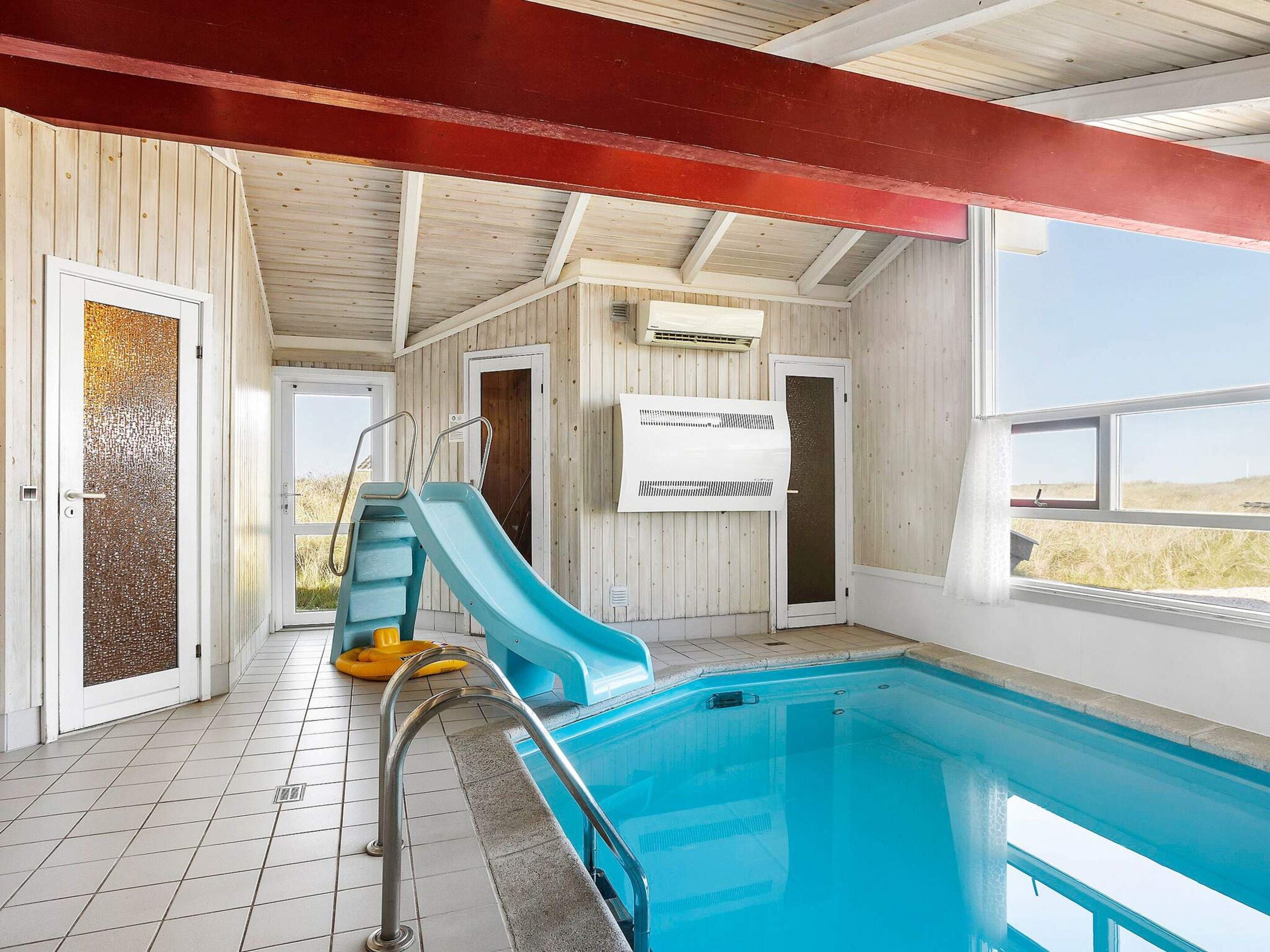An indoor swimming pool with a slide, tiled floor, and wooden walls.