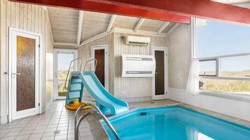 An indoor swimming pool with a slide, tiled floor, and wooden walls.