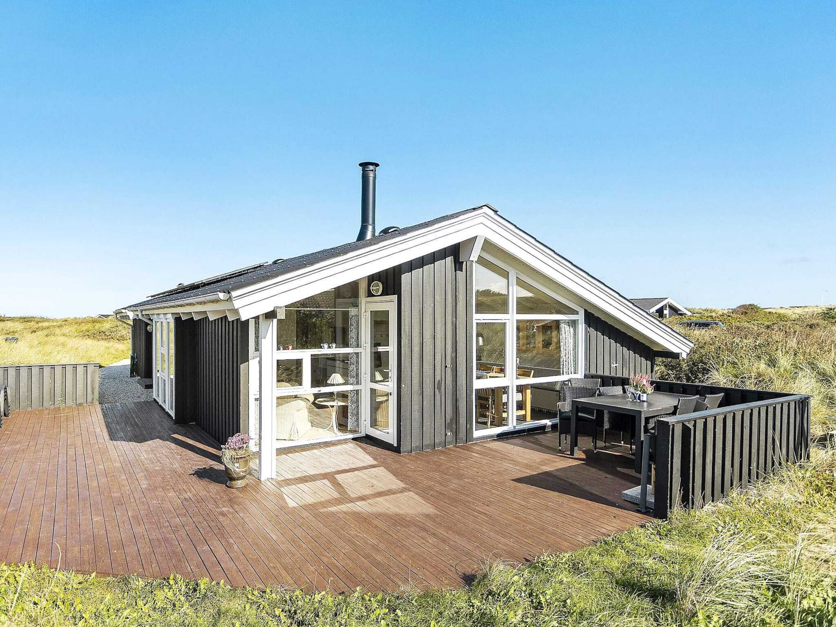 A modern house with a wooden deck, large windows, and a chimney.