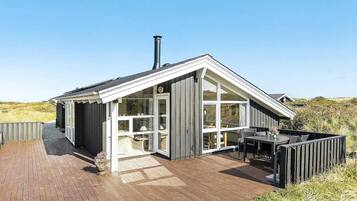 A modern house with a wooden deck, large windows, and a chimney.