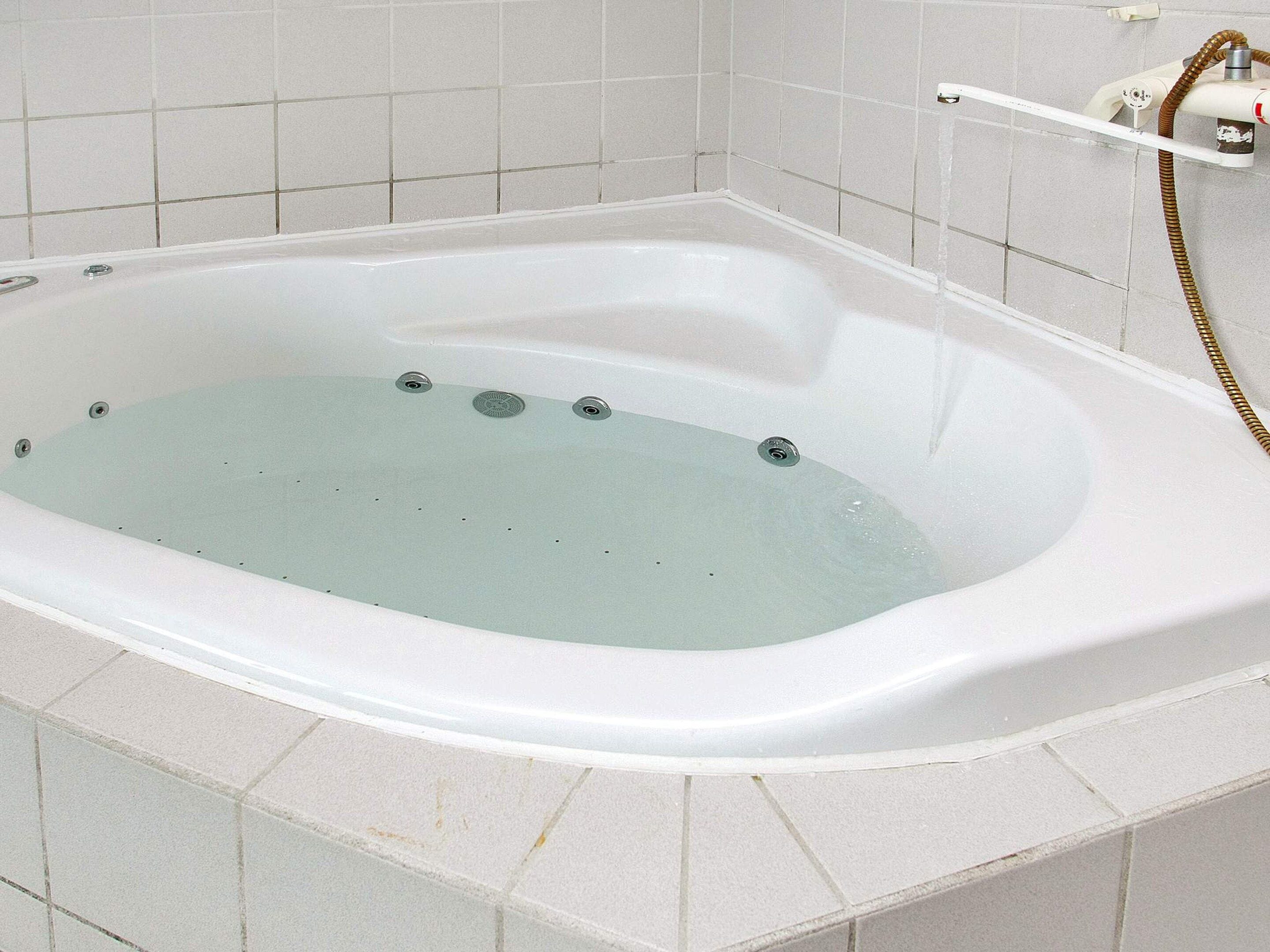 A white bathtub with a built-in seat, a handheld showerhead, and a control panel on the wall.